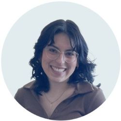 A headshot of Gloria, a Latina with black curled hair and glasses, smiling