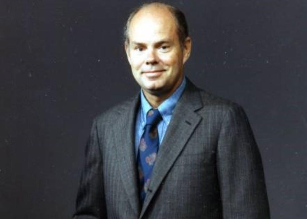 An image of Dr. Braddock during his time as professor at the University of Illinois. He is standing against a gray background with a dark gray pin-stripe suit and a blue tie.