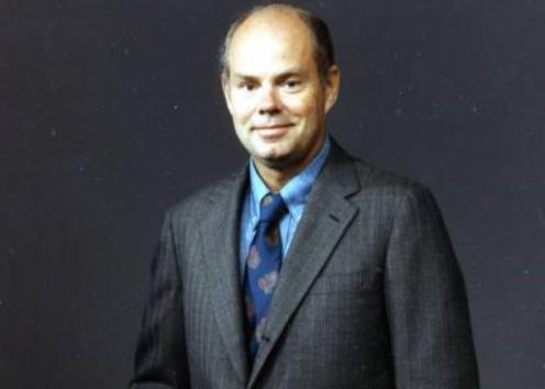 An image of Dr. Braddock during his time as professor at the University of Illinois. He is standing against a gray background with a dark gray pin-stripe suit and a blue tie.