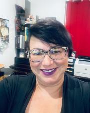 An image of Jeanette Cordova, a middle-aged Puerto-Rican woman with short black hair, glasses, and purple lipstick. 