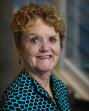 An image of Valerie, an older woman smiling with a teal and black polka-dotted blouse, ands short curly blonde hair.